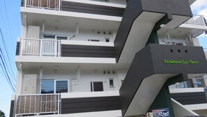 A multi-story residential building with balconies, a sign indicating 'Residencial Las Flores', and a visible window with a view of the sky.