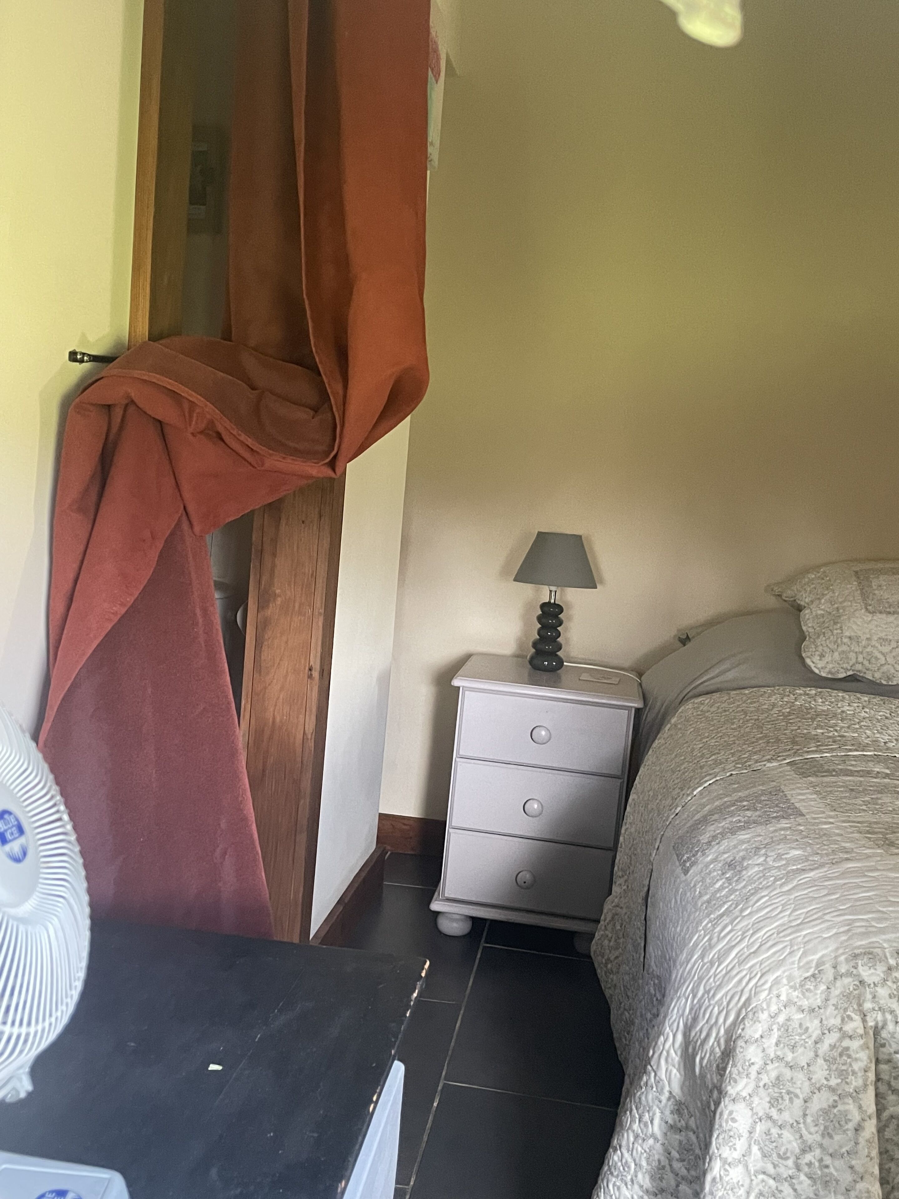 A bedroom with a bed, a nightstand, a lamp, a window with curtains, and a door.