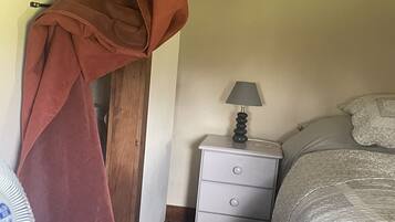 A bedroom with a bed, a nightstand, a lamp, a window with curtains, and a door.