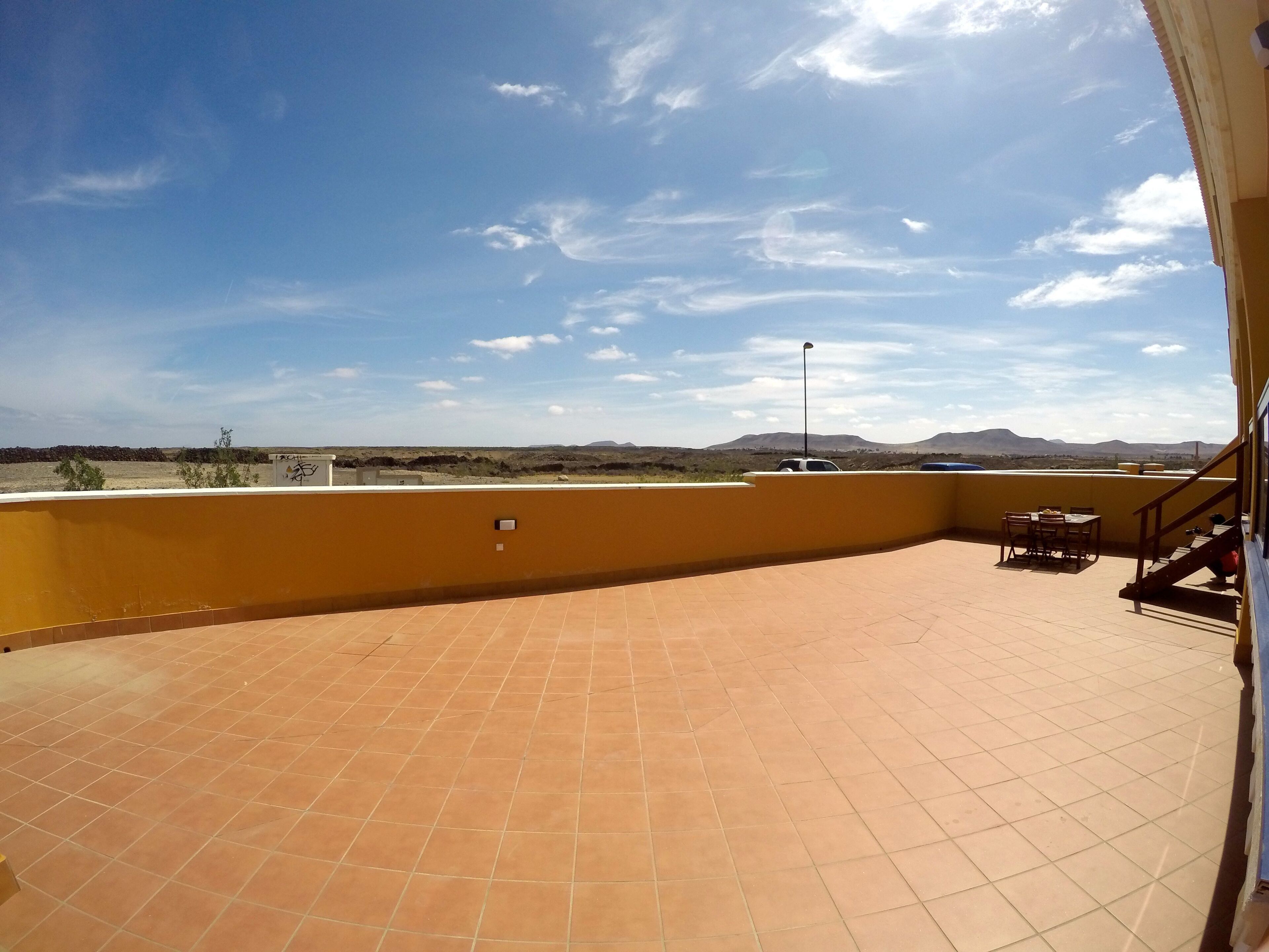 Une terrasse sur le toit, dotée d’un sol carrelé, d’une table et de chaises, et offrant une vue sur un paysage désertique avec des montagnes à l’horizon.