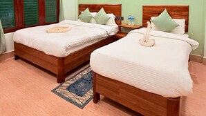 Habitación de hotel con dos camas de madera, cada una con colcha y almohadas blancas, una mesita de noche pequeña con una botella, y un ventilador de techo.