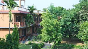 Un edificio de dos pisos con balcón, rodeado de abundante follaje y un jardín cuidado.