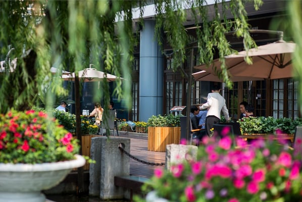 An outdoor seating area with tables and chairs, surrounded by potted plants and flowers.
