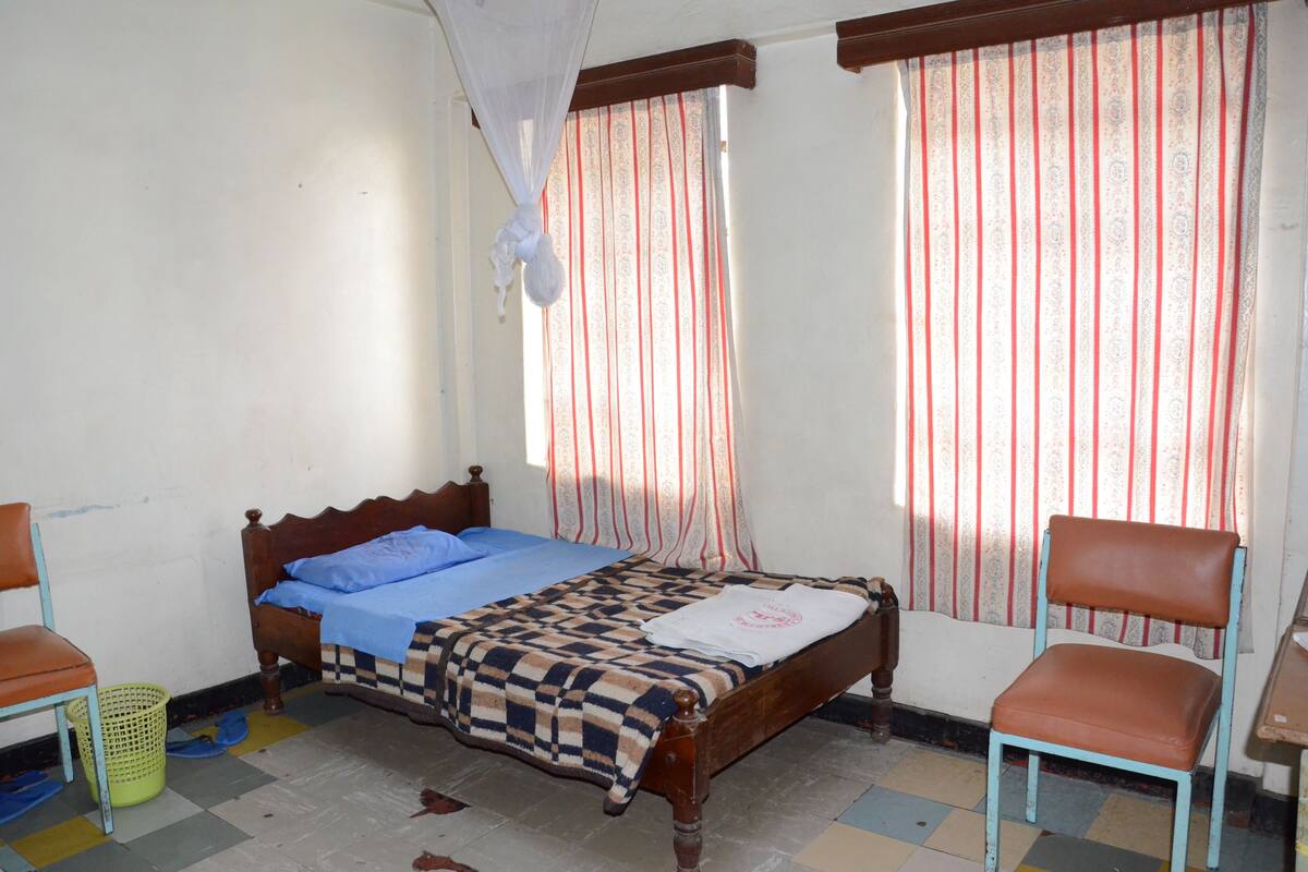 Um quarto com uma cama, uma cadeira, uma mesa e cortinas.