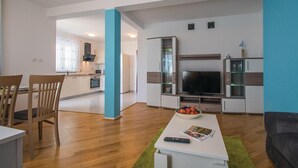 A modern living room with a flat-screen TV, a coffee table with a bowl of fruit, and a dining area with chairs and a table. - Stunning apartment in Labin with house sea view (Labin)