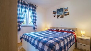 A bedroom with a checkered bedspread, a window with curtains, bedside lamps, and wall art. - Stunning apartment in Labin with house sea view (Labin)