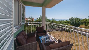 A balcony with wicker furniture, a table with cups and a book, and a view of the sea and greenery. - Stunning apartment in Labin with house sea view (Labin)