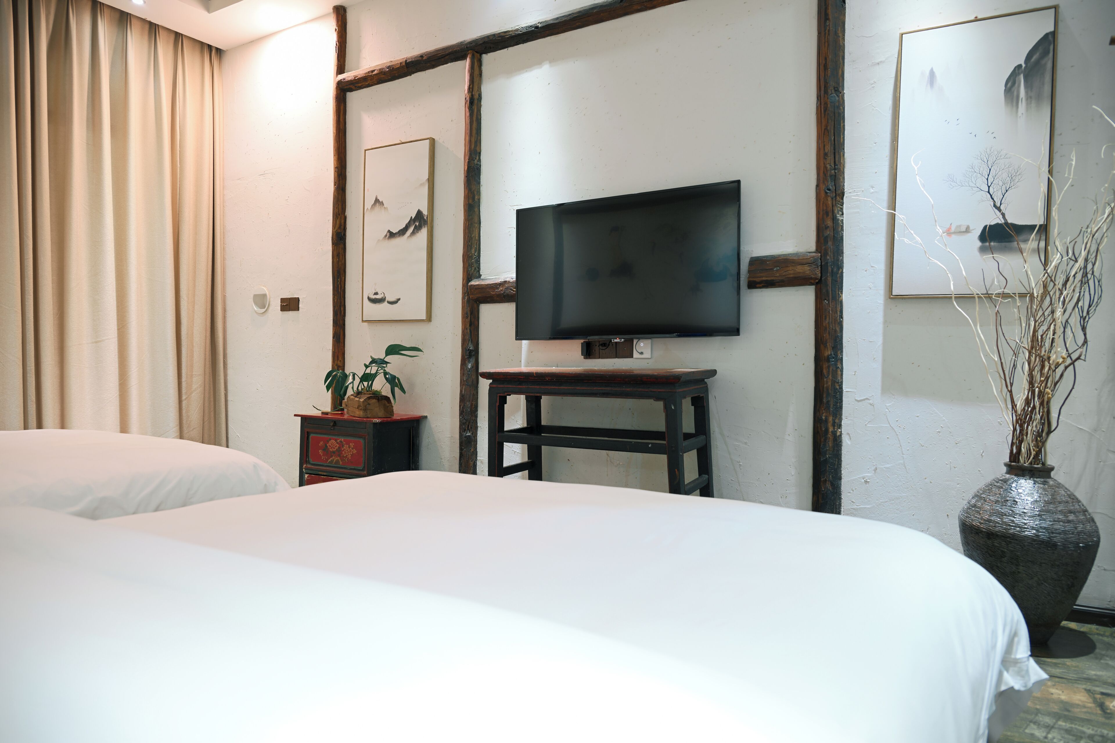 Ett hotellrum med två sängar, en tv på ett träställ, en vas med grenar och konstverk på väggarna.