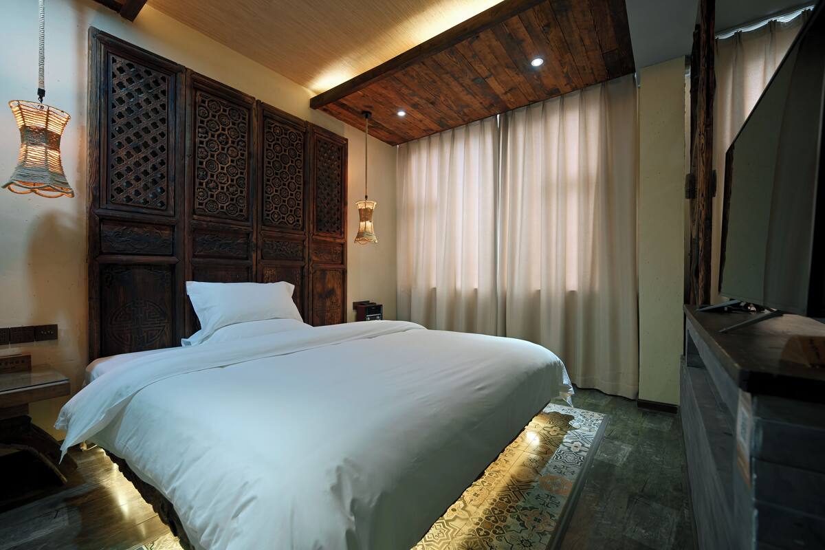 A neatly made bed with a wooden headboard, a bedside table, and a patterned rug.