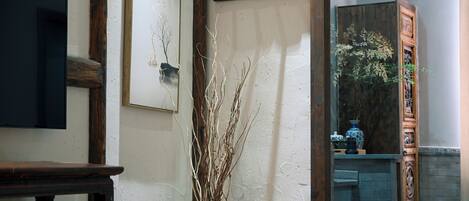 A room with a wooden table, a vase with dried branches, and a mirror reflecting a cabinet with decorative items.