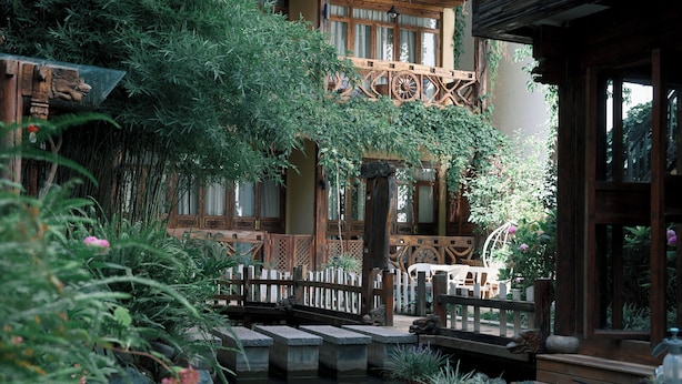 A traditional wooden building with a garden featuring a pond, stone bridge, and lush greenery.