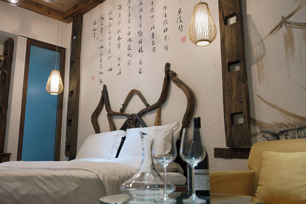 A bedroom with a bed, bedside table, and a wall with calligraphy.