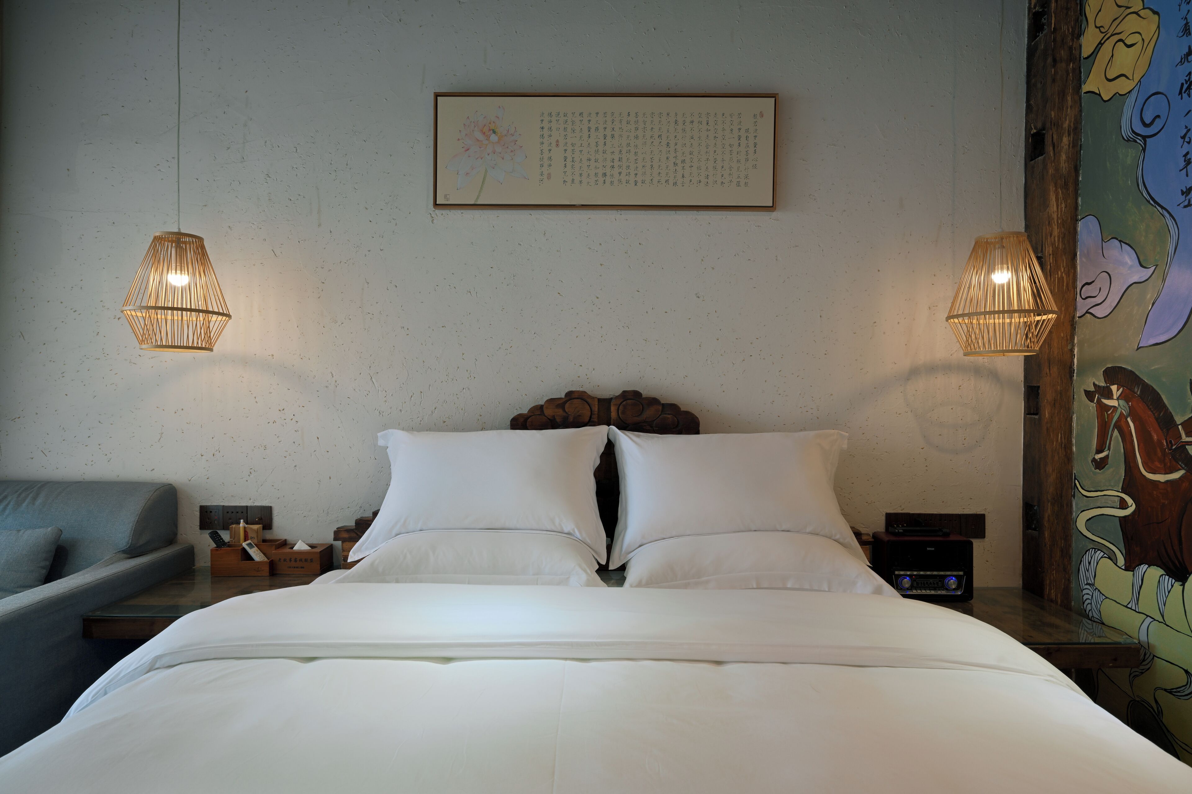 Una habitación de hotel con una cama grande, dos lámparas de noche, un cabecero de madera, una mesita con una radio y un mural de colores en la pared.