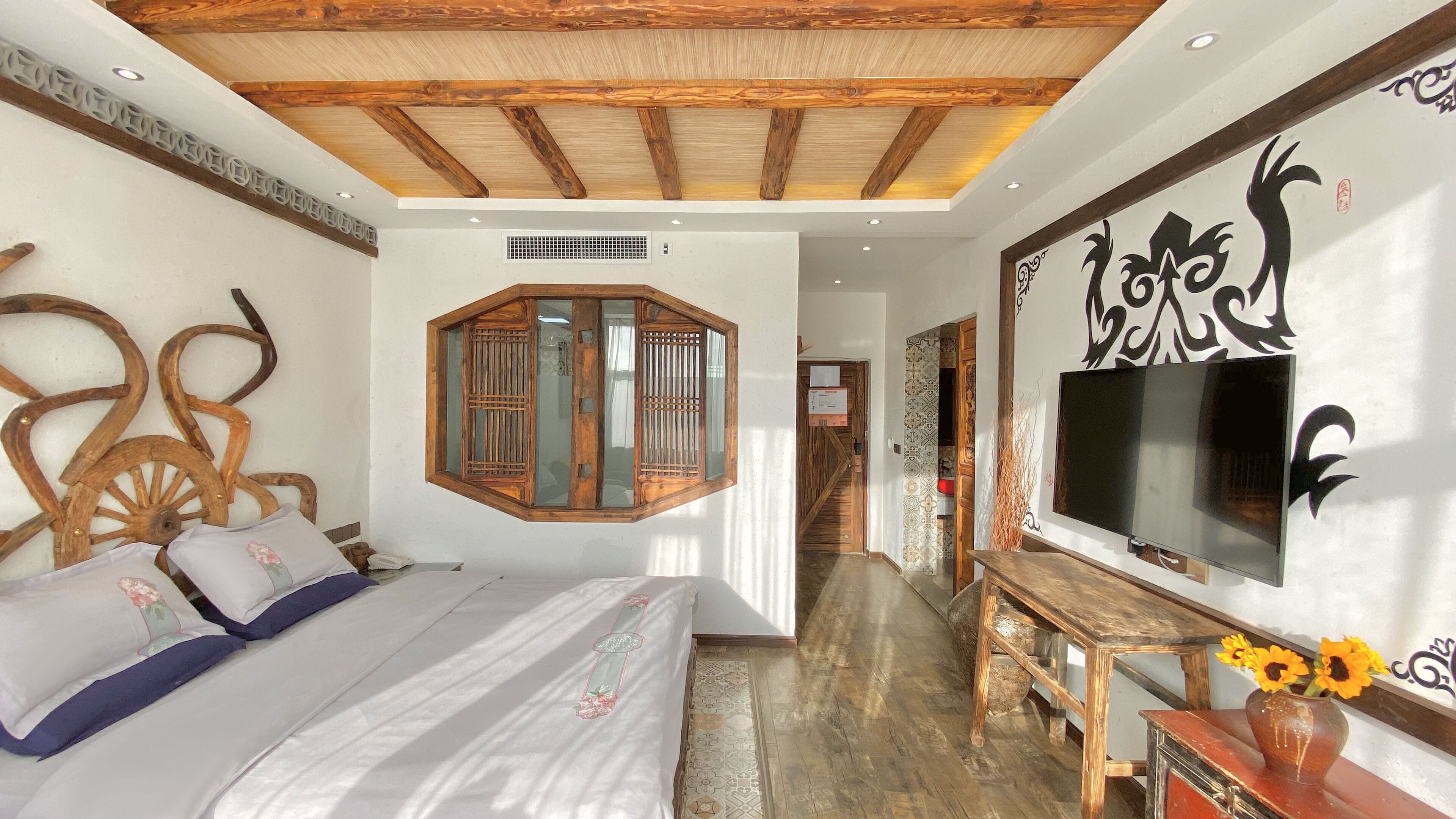 A bedroom with a large bed, a wooden ceiling, a TV, and a decorative wall piece.
