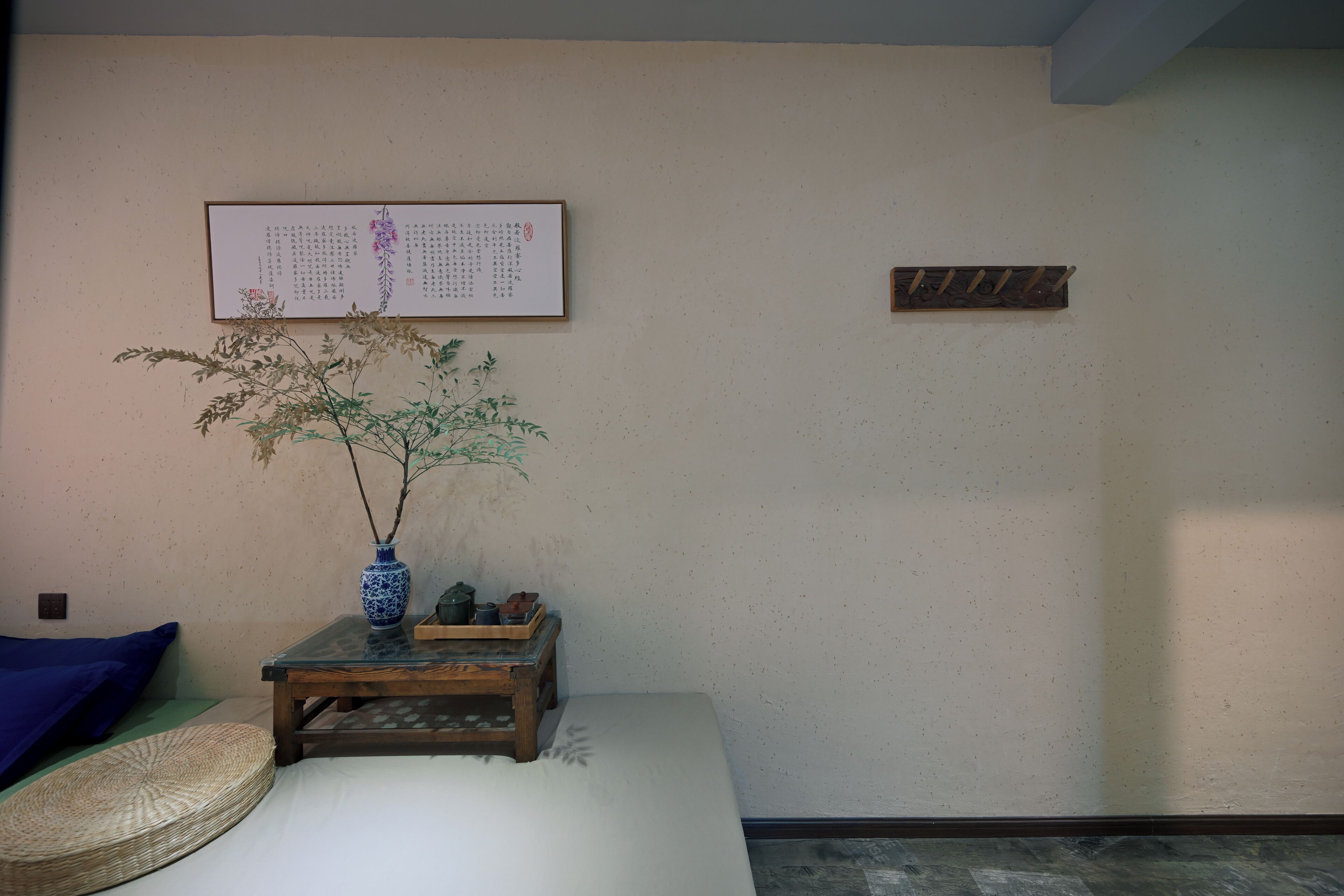 Une pièce de style japonais traditionnel, avec un sol recouvert de tatamis, une basse table en bois, un vase bleu orné d’une branche et une œuvre calligraphique encadrée accrochée au mur.