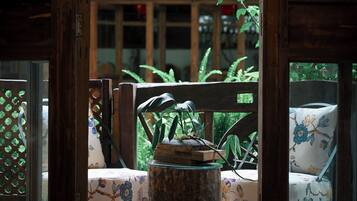 A wooden chair with a floral cushion, a glass table, and a wooden stool with a plant.