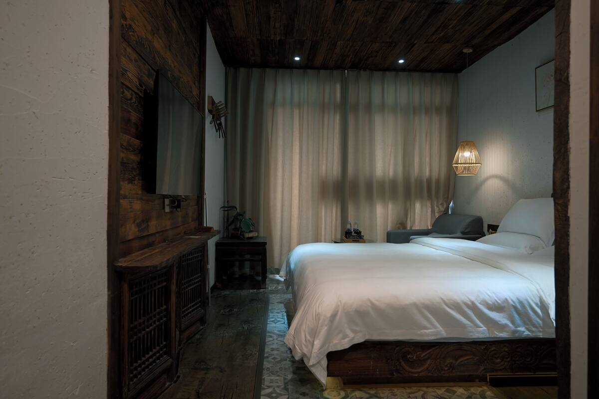 A bedroom with a wooden ceiling, a bed with white bedding, a nightstand, and a wall-mounted lamp.