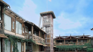 A traditional multi-story building with wooden balconies, a central tower, and a small pond with a statue.