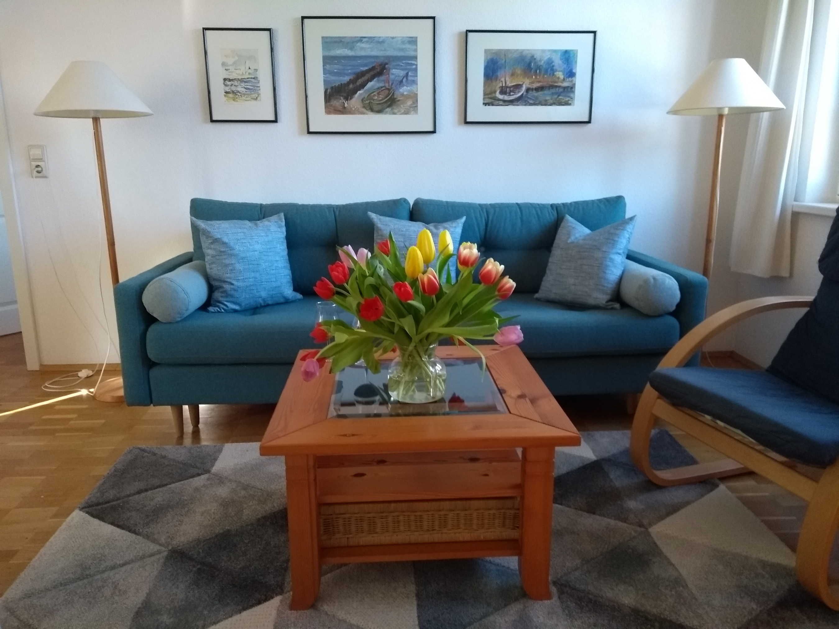 Un salon avec un canapé bleu, une table basse en bois sur laquelle est posé un vase de tulipes, et deux lampadaires.