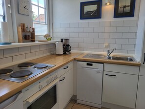 A compact kitchen with a Siemens oven, a coffee maker, a dishwasher, and a window with blinds.