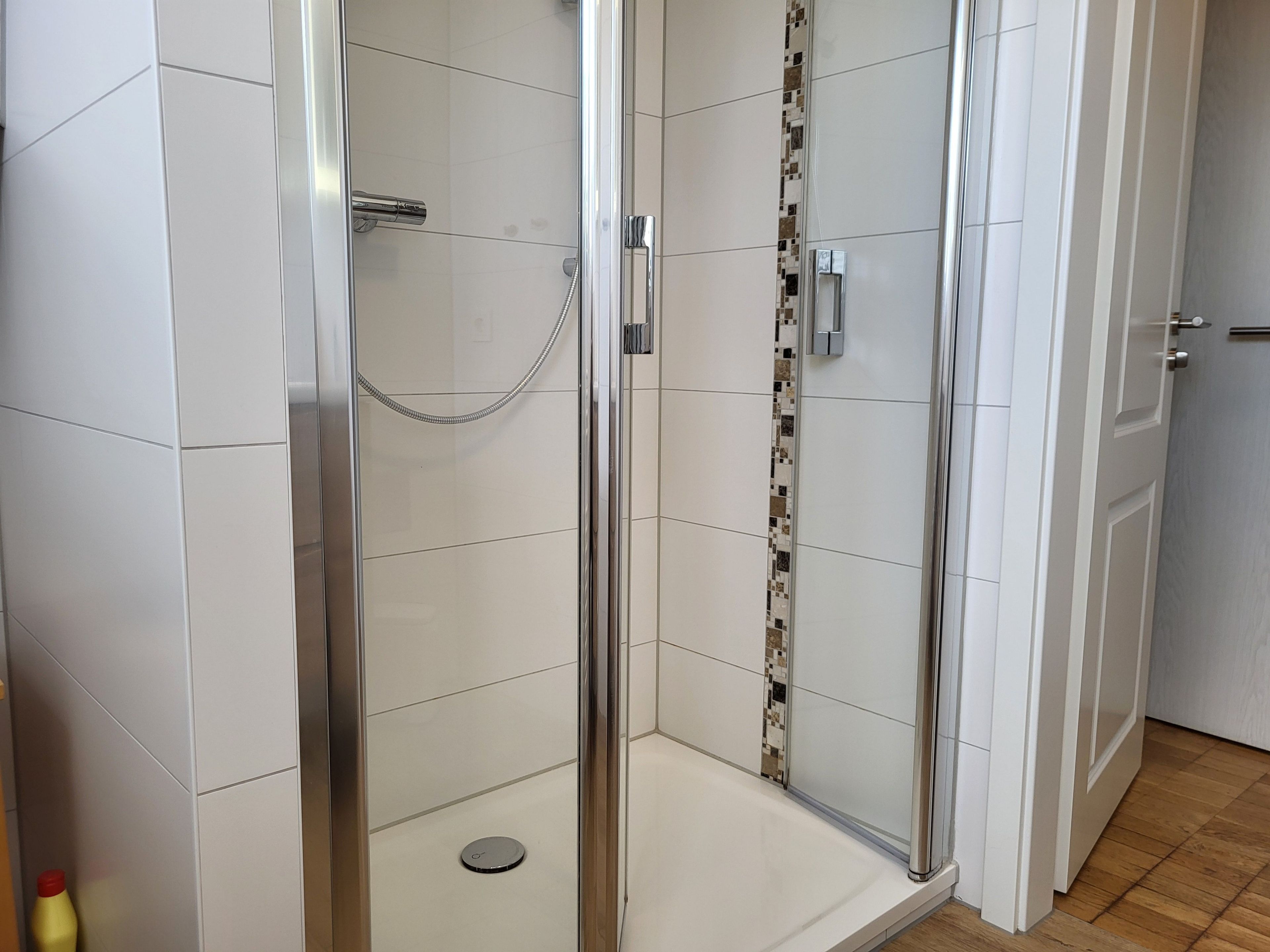 Une douche fermée par des parois de verre, dotée d’un sol carrelé, d’un pommeau de douche et d’un panneau de commande.