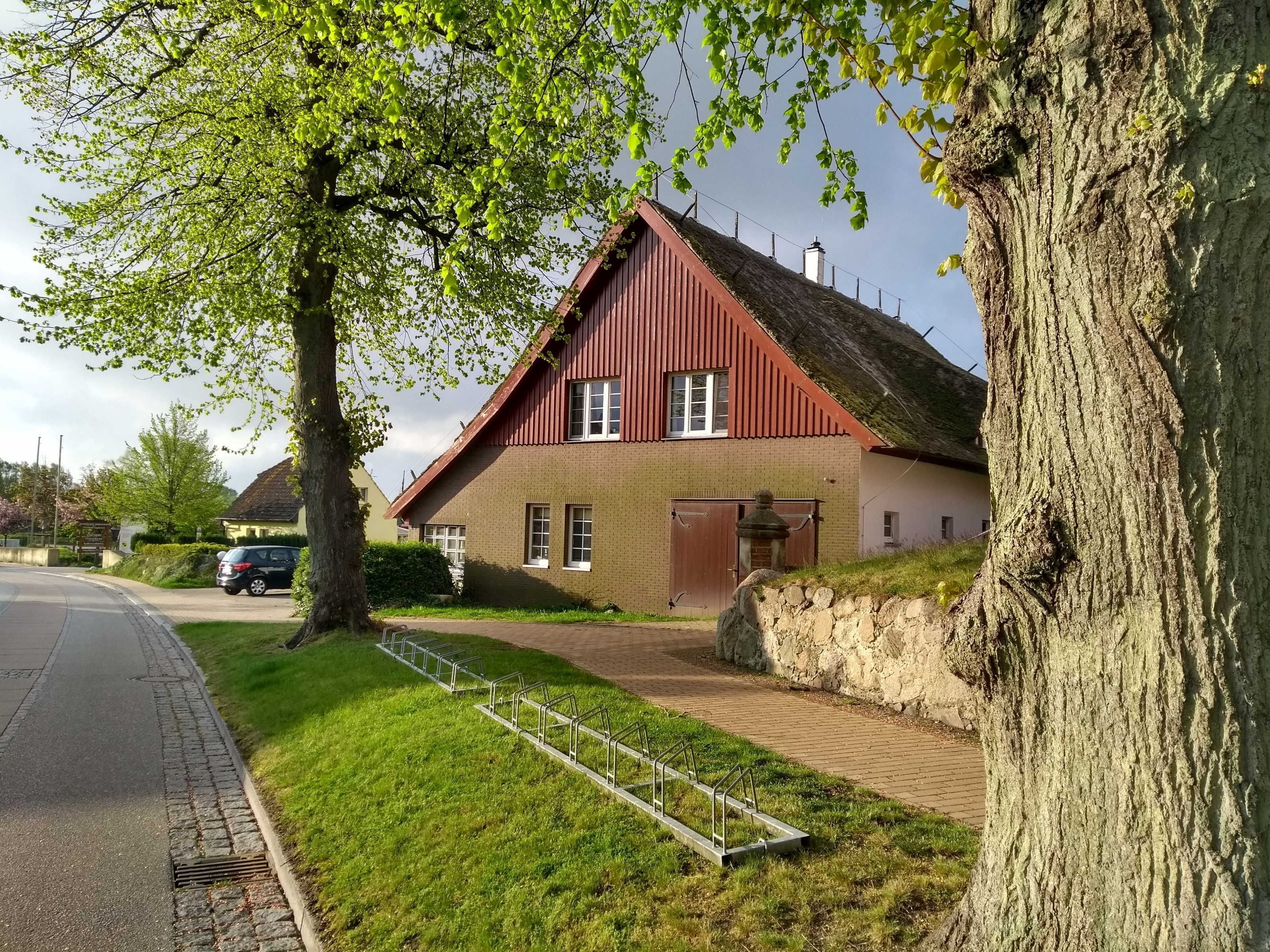 Une maison avec un toit rouge, une allée pavée et un porte-vélo en métal.