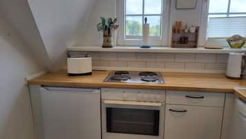 Een keuken met een vaatwasser, fornuis, oven en een raam met een klok.