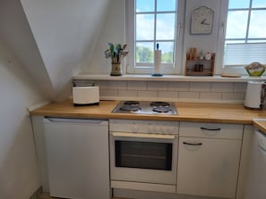 A kitchen with a dishwasher, stove, oven, and a window with a clock.