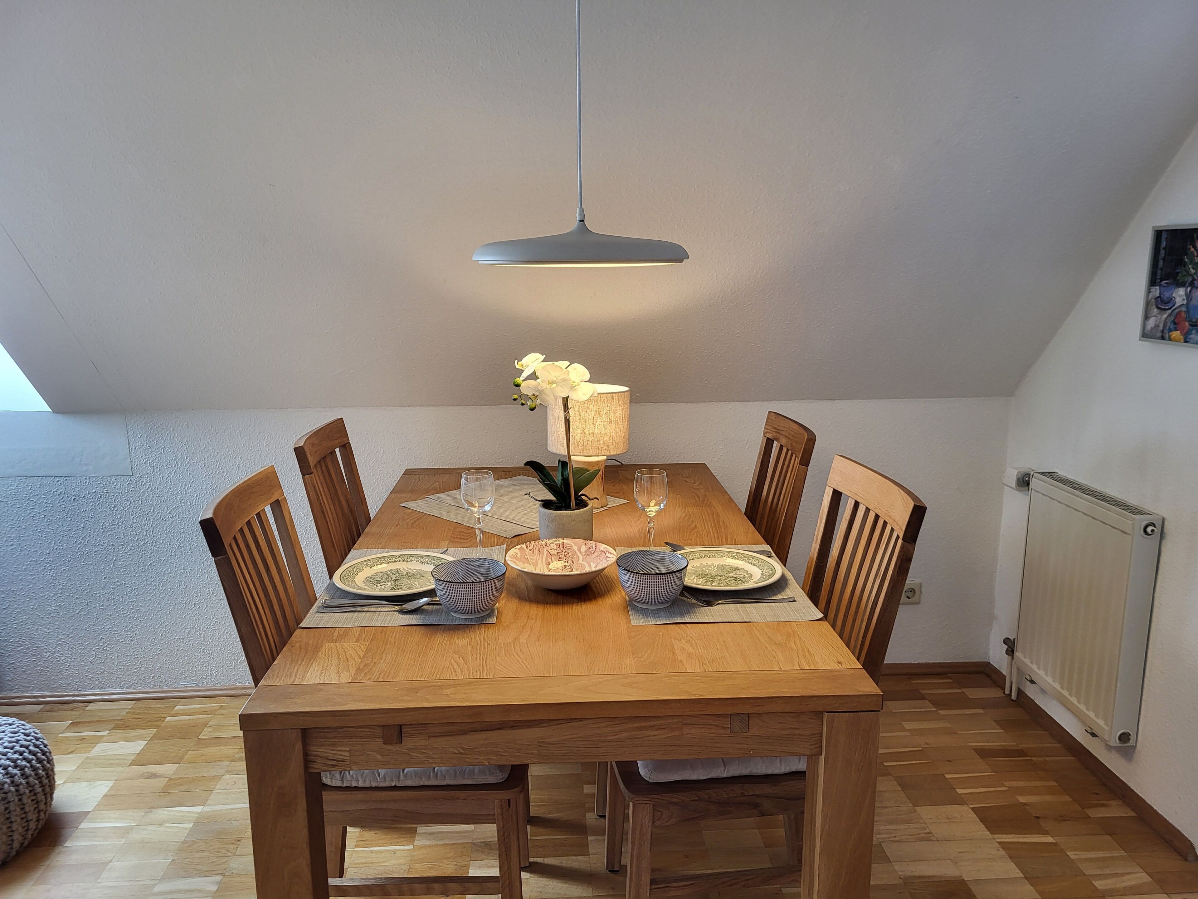 Un coin repas avec une table en bois, des chaises, un luminaire suspendu et un radiateur fixé au mur.