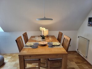 A dining area with a wooden table, chairs, a hanging light fixture, and a radiator on the wall.