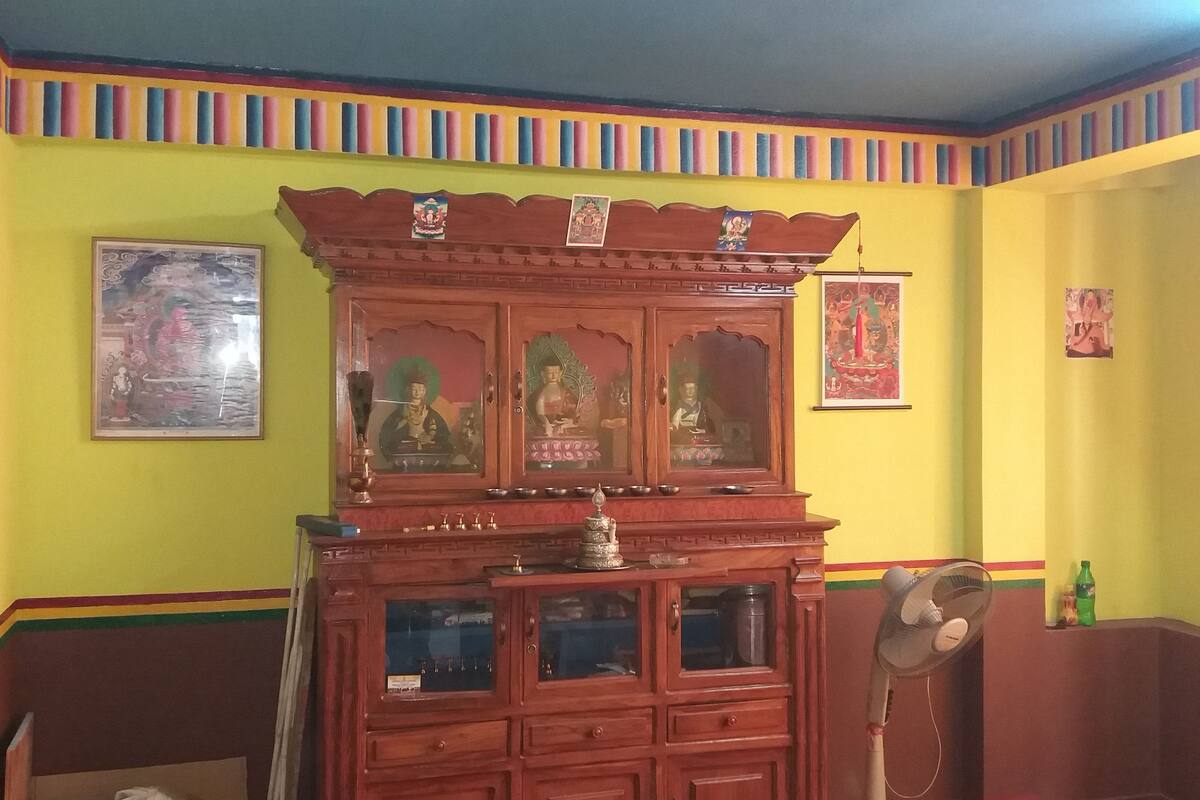 A room with a wooden cabinet with glass doors, a fan, and religious paintings on the walls.