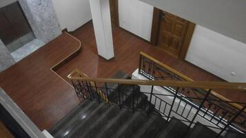 A staircase with a wooden handrail and black railings, leading to a landing with a marble wall and a wooden door.