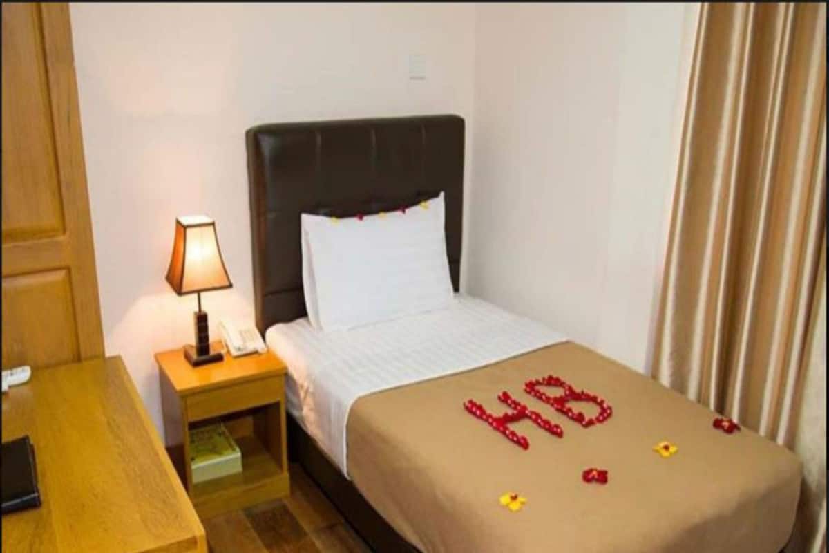 A hotel room with a bed, a nightstand, a lamp, and a wooden desk.