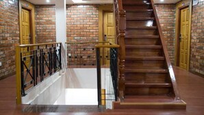 Una escalera con escalones de madera y barandillas de metal, rodeada de muros de ladrillo y puertas de madera.