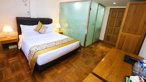 Una habitación de hotel con cama, lámparas de noche, un escritorio de madera y un armario.
