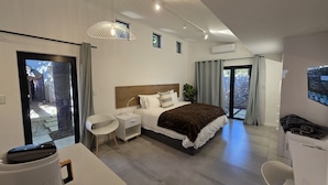 Een moderne hotelkamer met een groot bed, nachtkastjes, een bureau en een stoel. Er is uitzicht op het exterieur door een schuifdeur.