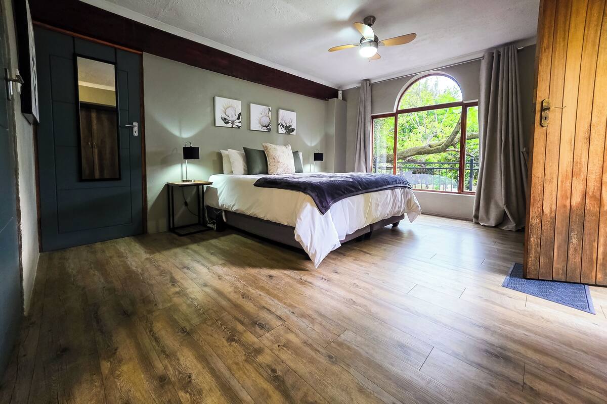 Un dormitorio con cama, ventilador de techo, ventana con vistas y una puerta.