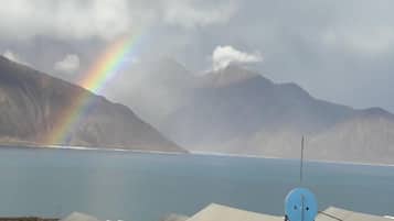 A satellite dish, tents, and a mountain range with a rainbow over a body of water.