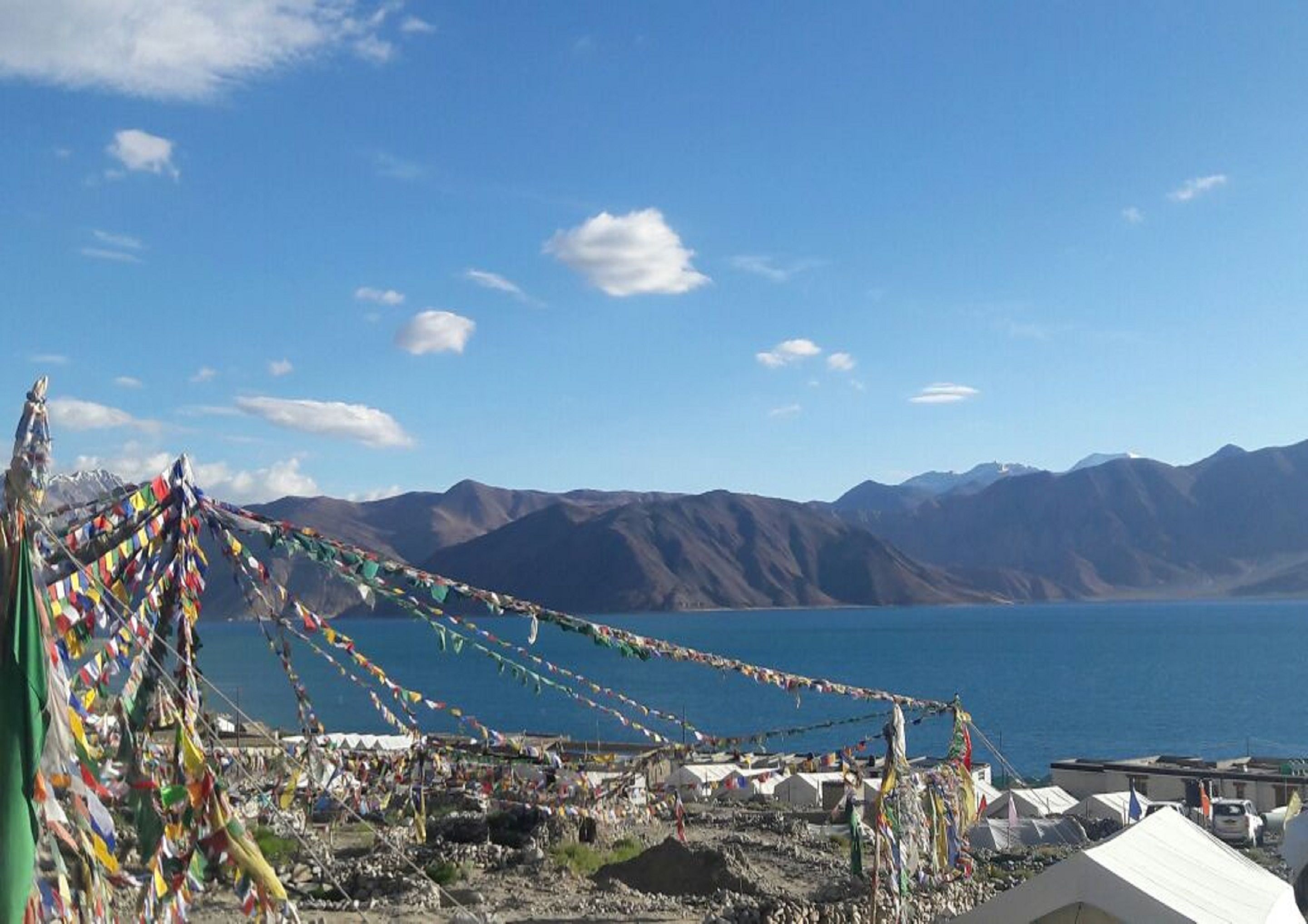 A mountainous landscape with a clear sky, a body of water, and colorful prayer flags.