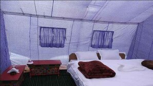A room with a bed, a small table, and a chair. There is a window with a mesh screen. - Eco Travellers Camp (Leh)
