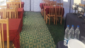A tented dining area with multiple tables and chairs, a patterned floor, and water bottles on a table. - Eco Travellers Camp (Leh)
