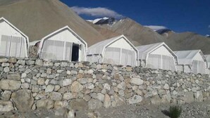 A row of white, semi-transparent tents with stone walls, set against a mountainous backdrop. - Eco Travellers Camp (Leh)