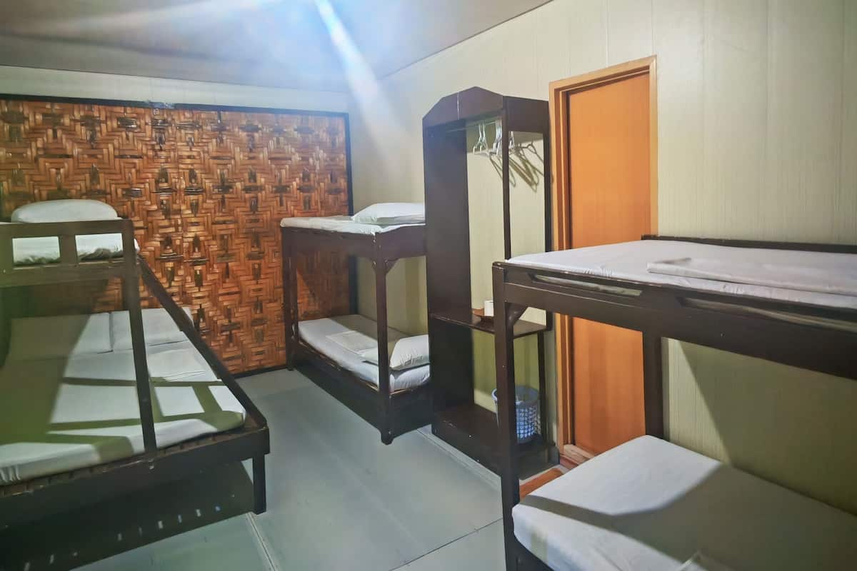 A dormitory room with bunk beds, a wooden wall panel, a small table, and a door.