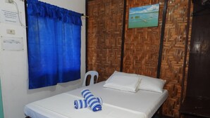Una cama con ropa blanca, dos almohadas a rayas, una cortina azul, un cabecero de madera y un cuadro con una playa.