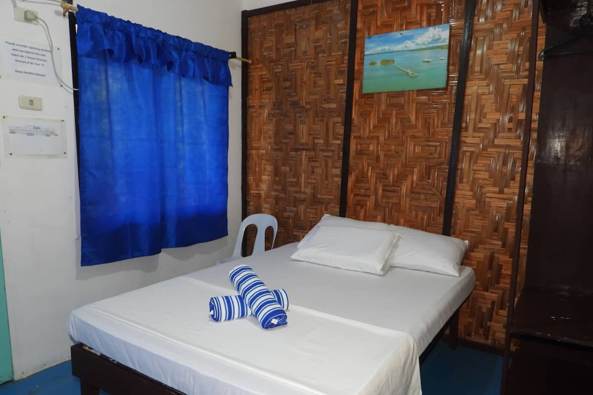 A bed with white bedding, two striped pillows, a blue curtain, a wooden headboard, and a painting of a beach scene.