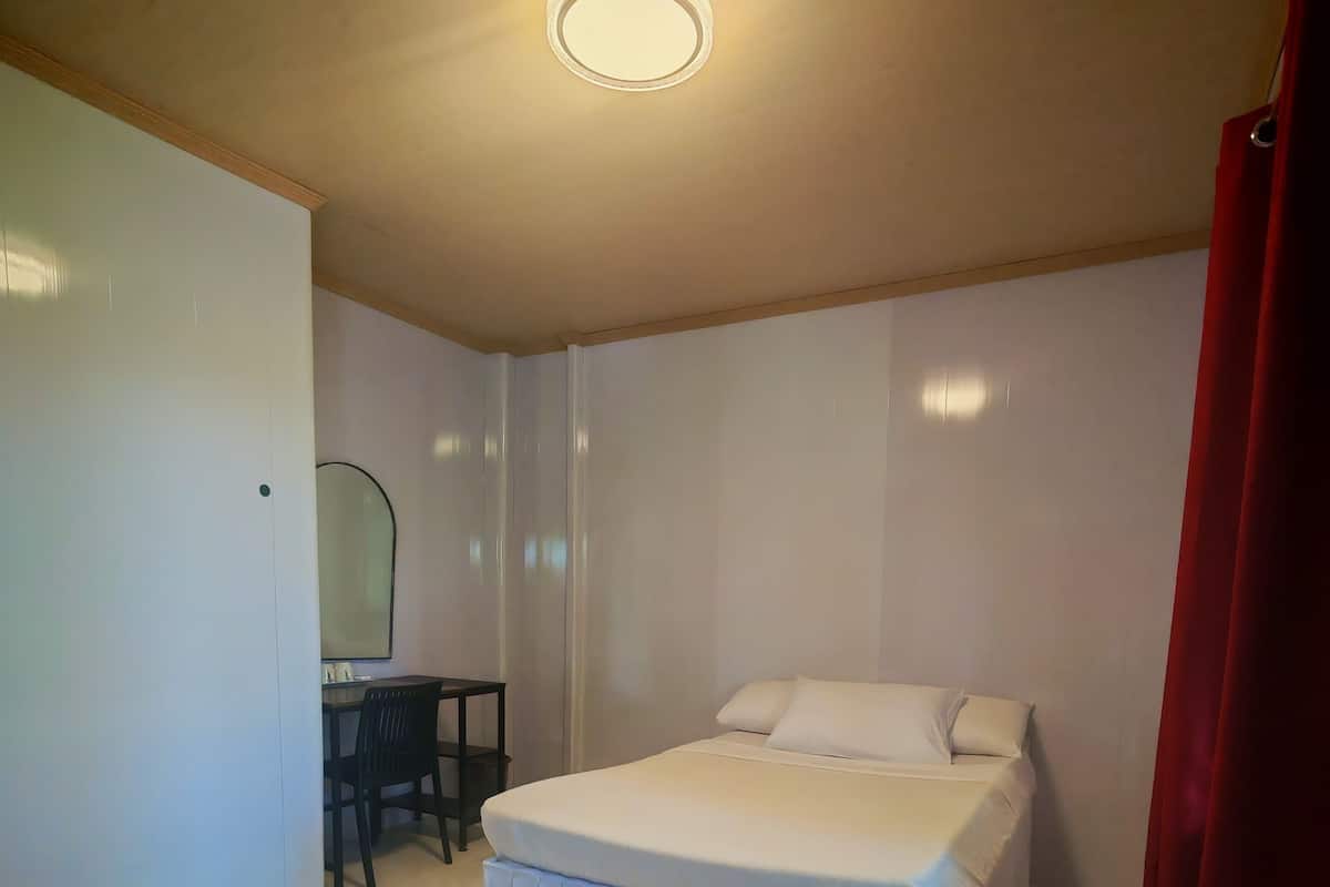 A bedroom with a bed, a desk, a chair, a mirror, and a red curtain.