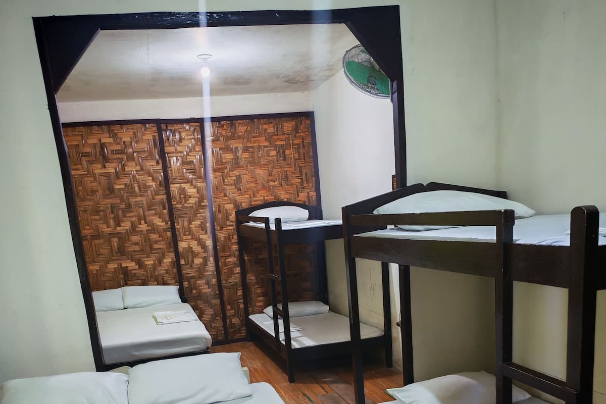 A room with bunk beds, a wooden wall panel, and a ceiling fan.