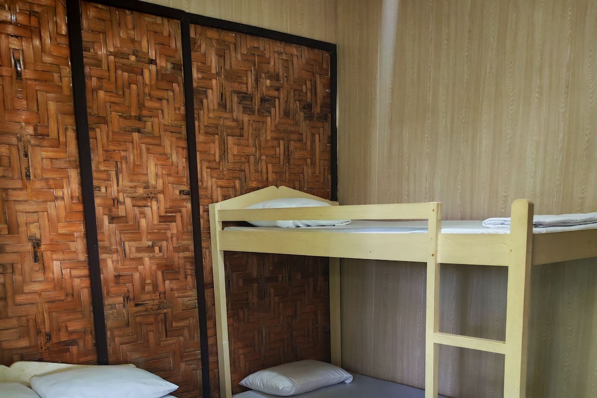 A bunk bed room with a wooden headboard, a lower bunk with a mattress and pillows, and a top bunk with a ladder.