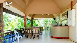 Un espacio al aire libre techado con una mesa de recepción, sillas de madera y una silla de plástico blanco.