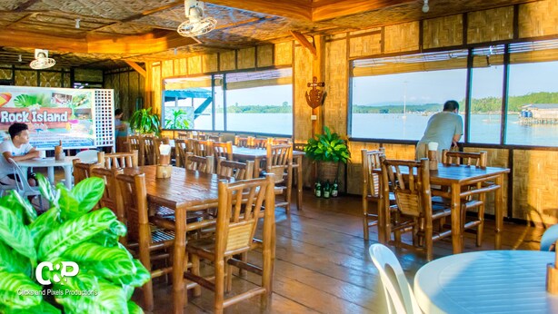 Un restaurante con mobiliario de madera y amplios ventanales con vista a un cuerpo de agua.